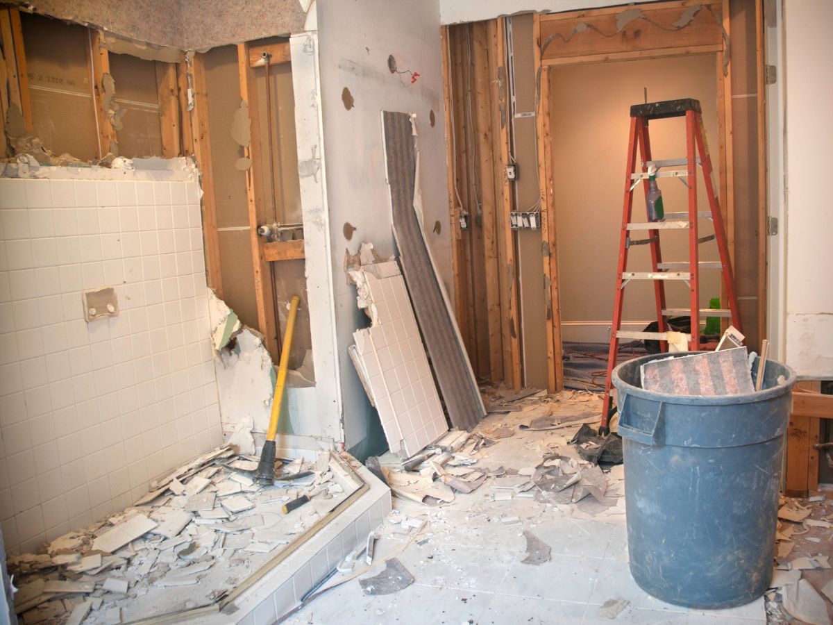 Bathroom stripped to the studs with broken tile and debris on the floor