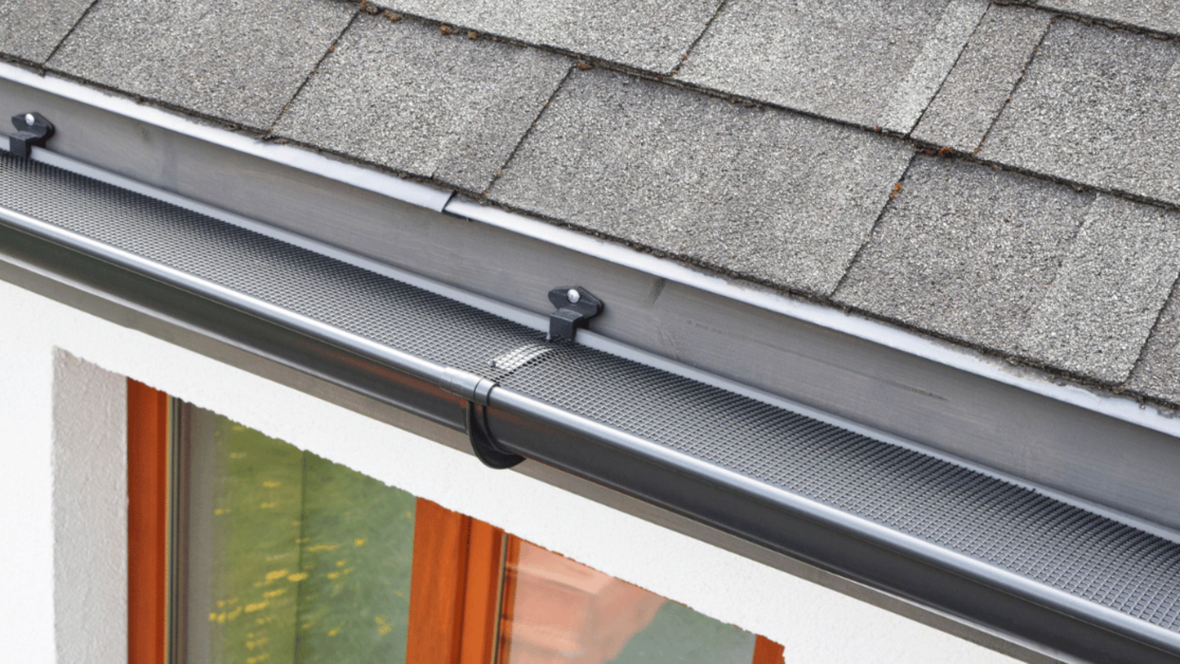 Mesh gutter guard installed along a shingled roof edge above a window