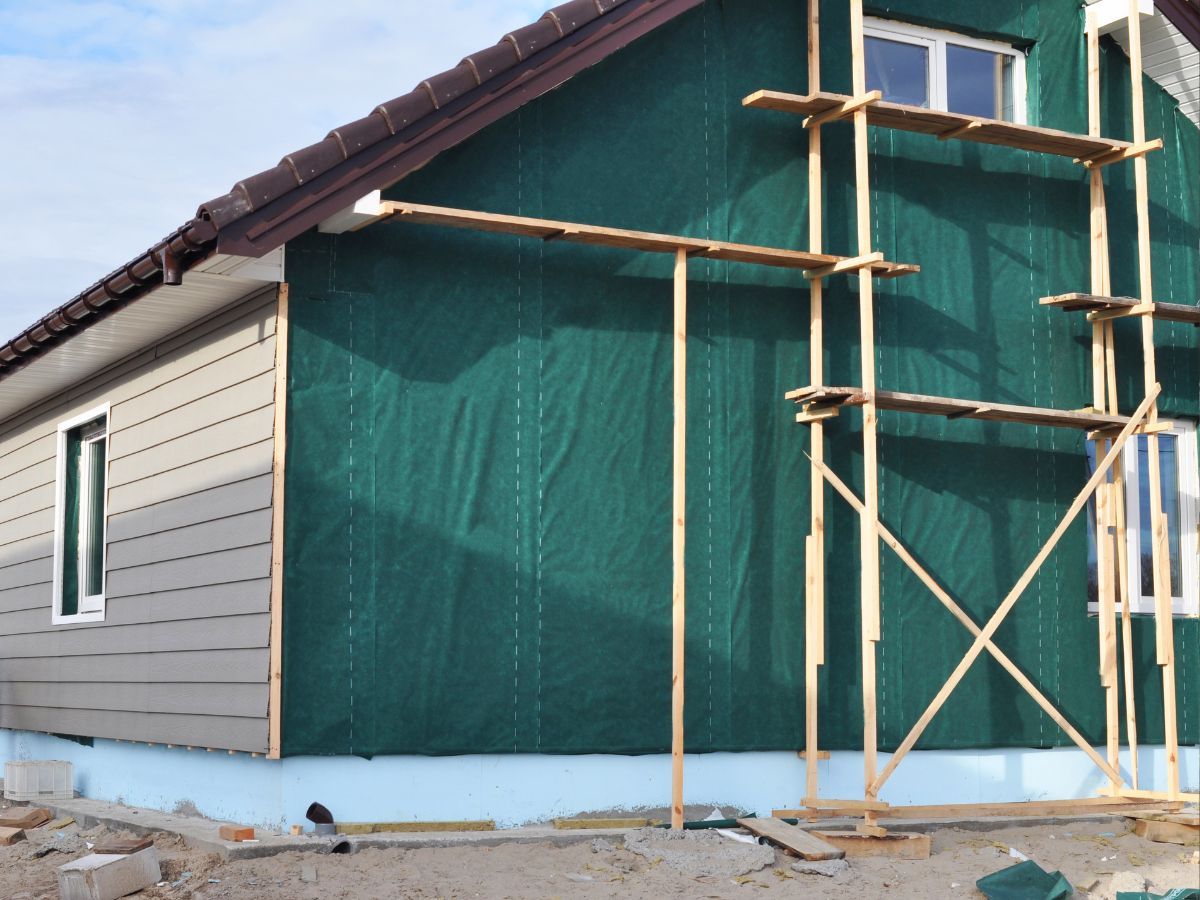 House wrapped in a green weather-resistive barrier with scaffolding and partial siding installed