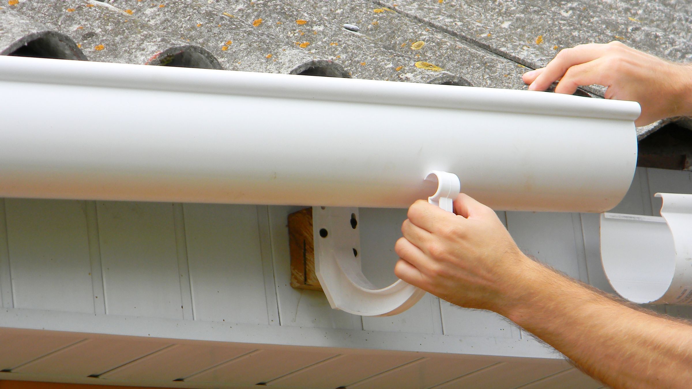 Half-round gutter being fitted into an external bracket on the fascia