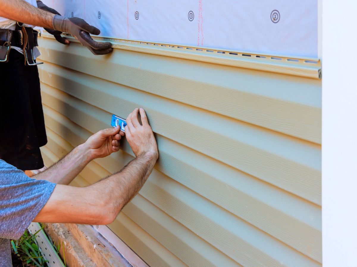 Installer fastening a vinyl siding panel over house wrap