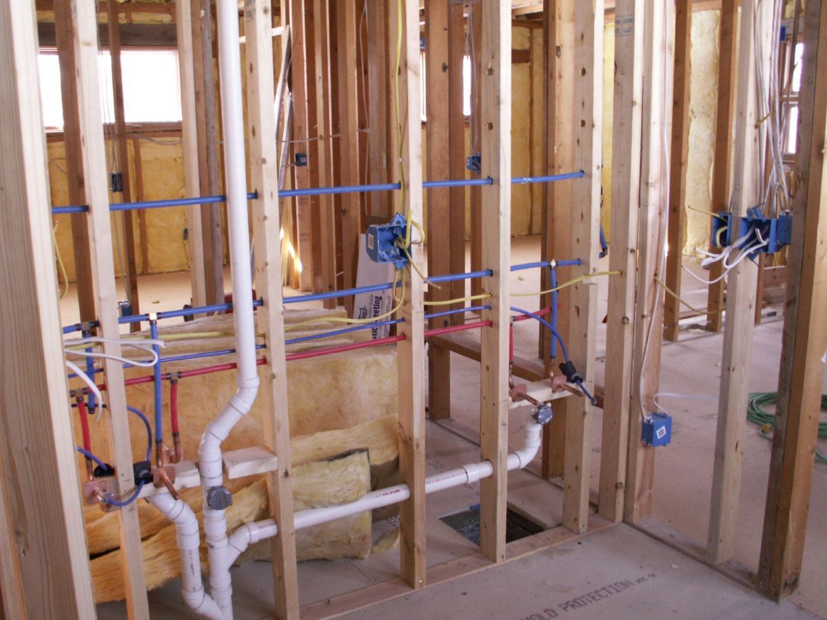 Open bathroom wall framing with PEX supply lines, drain pipe and electrical boxes