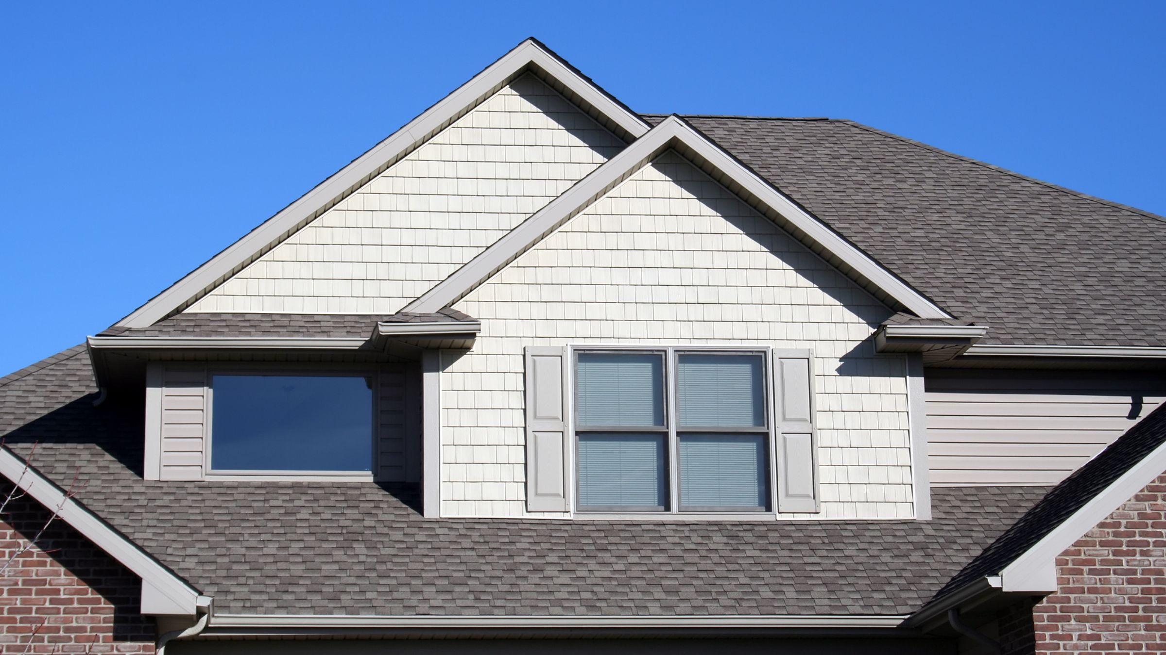 Gabled roofline with new architectural asphalt shingles against a clear blue sky