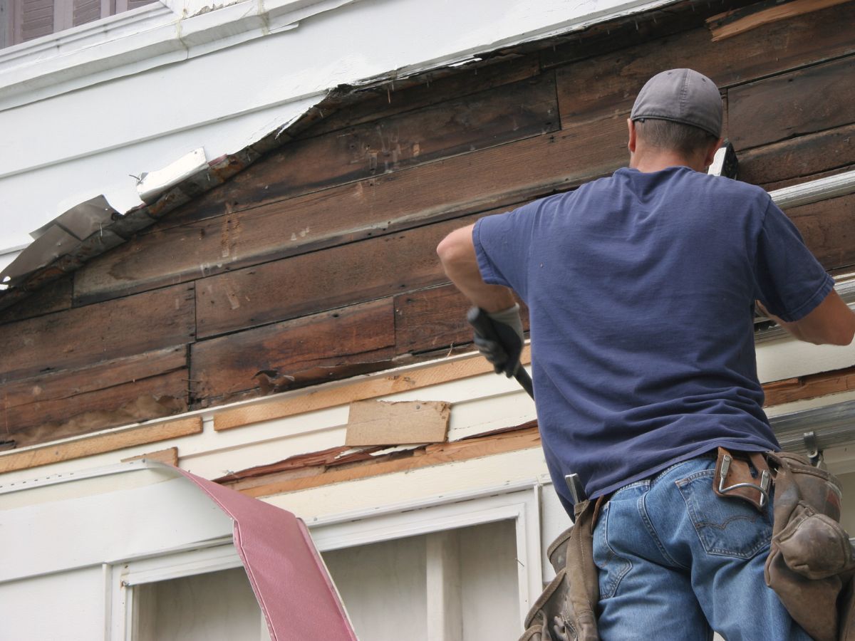 Worker prying old siding away from a wall, exposing the boards underneath