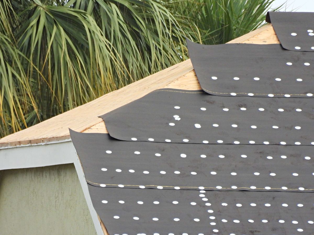 Synthetic underlayment rolled out and fastened across a bare roof deck