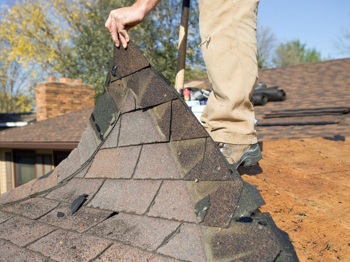 Roofer removing old shingles from a roof deck during tear-off