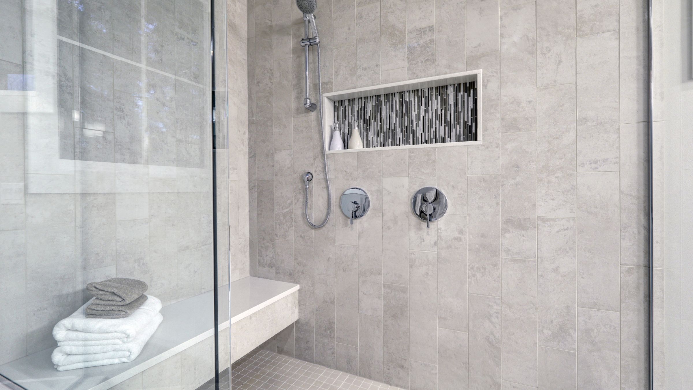 Modern tiled walk-in shower with a glass panel and recessed niche