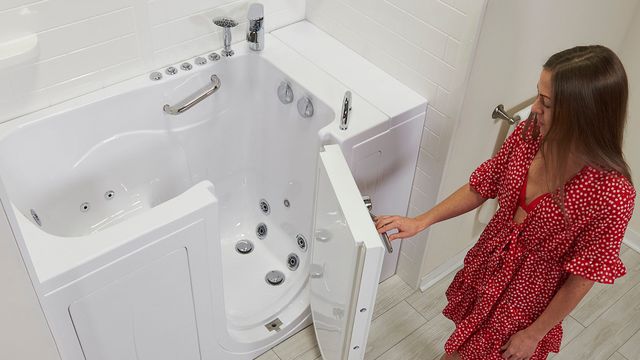 Woman opening the door of a white walk-in tub with jets in a tiled bathroom